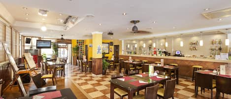 A hotel lobby with a checkered floor, multiple dining tables, chairs, a bar area, and a television screen.