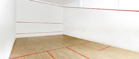 A squash court with white walls and a wooden floor marked with red lines.