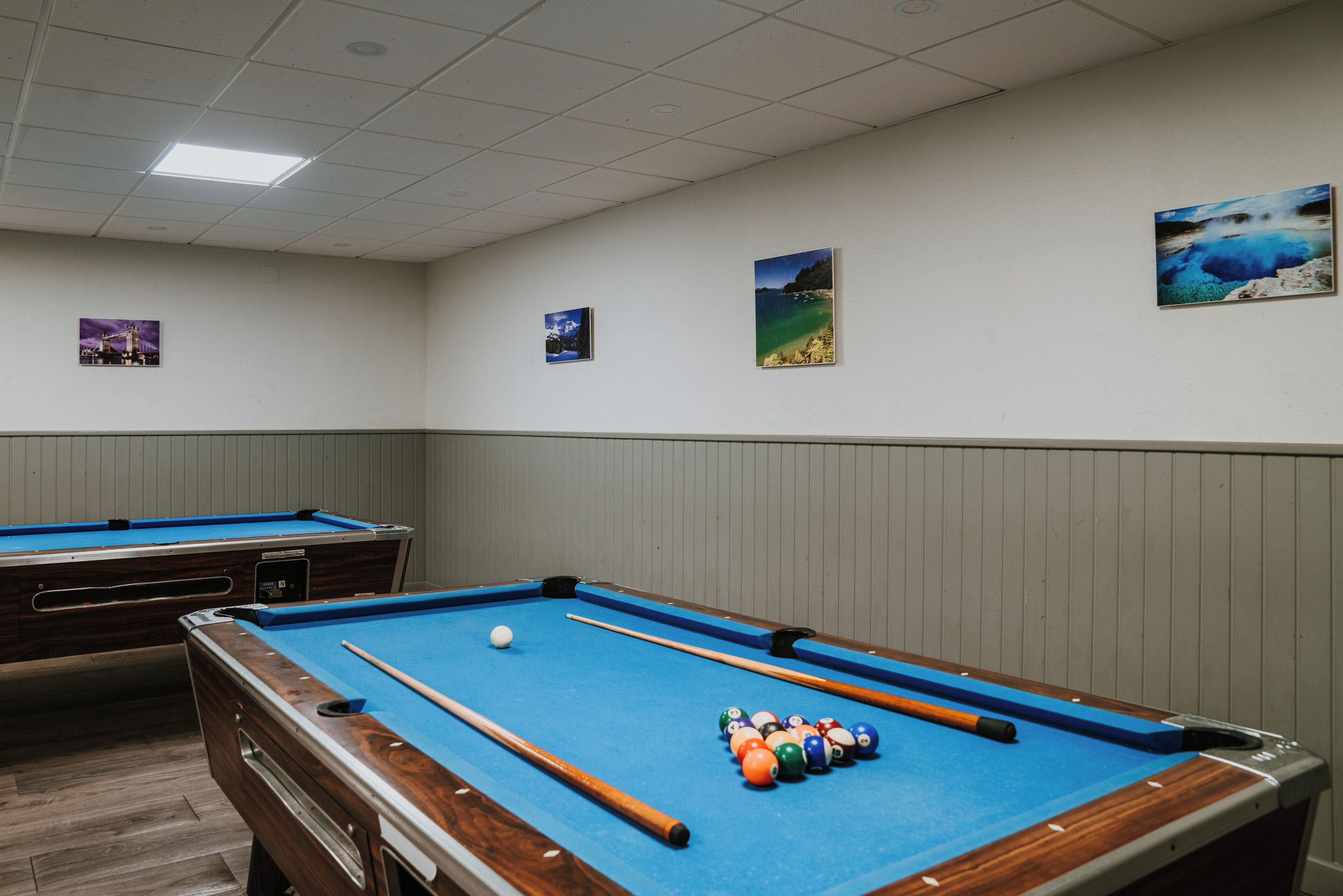 Une table de billard avec des billes et des queues, un plafond blanc et des tableaux encadrés accrochés au mur.