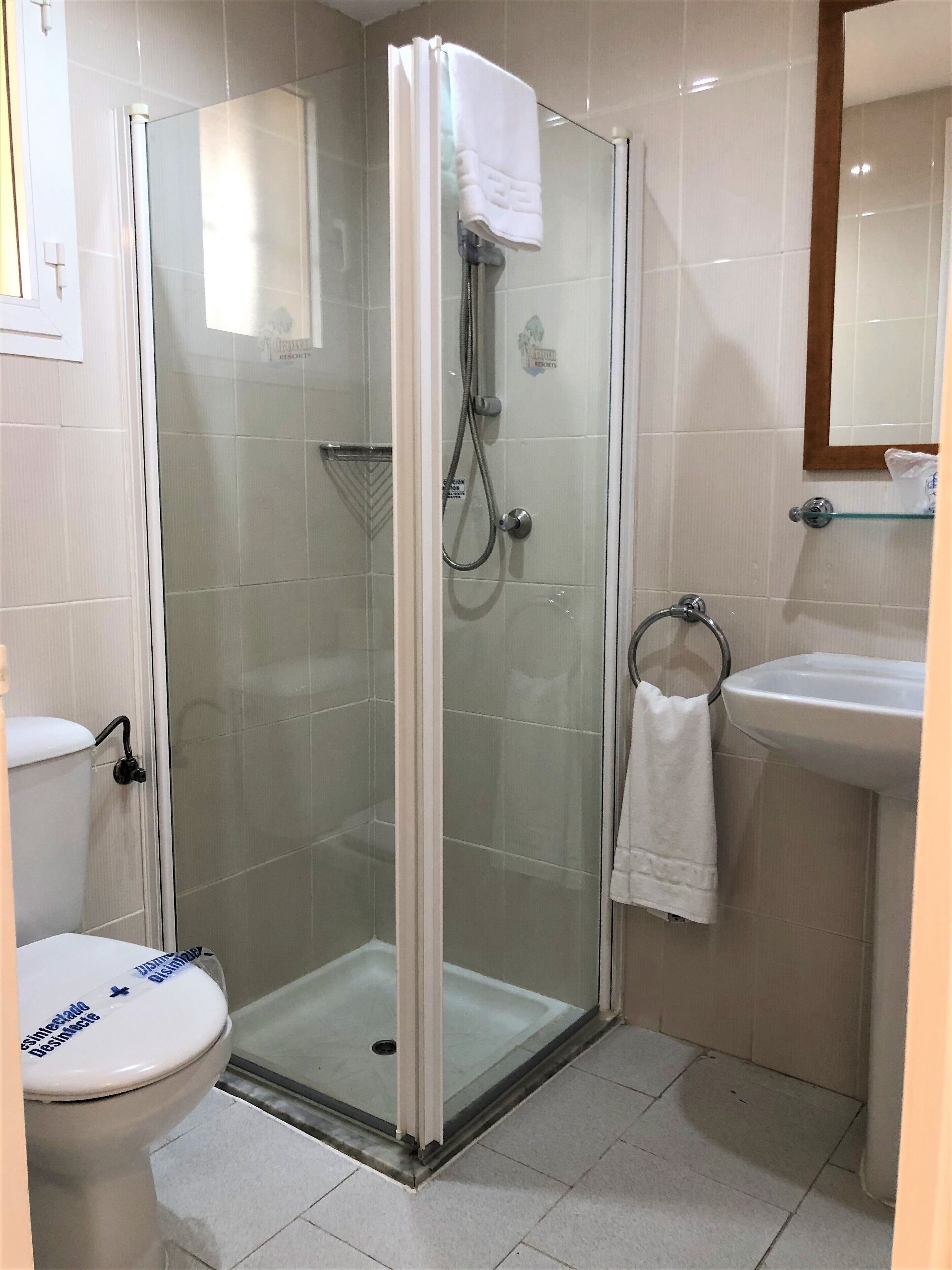 A modern bathroom with a glass-enclosed shower, a white toilet, and a sink with a towel hanging on the wall.