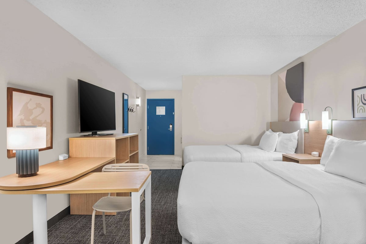 A hotel room with a bed, a desk, a chair, a TV, and a door.