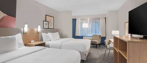 A hotel room with two beds, a desk, a TV, and a window with curtains.