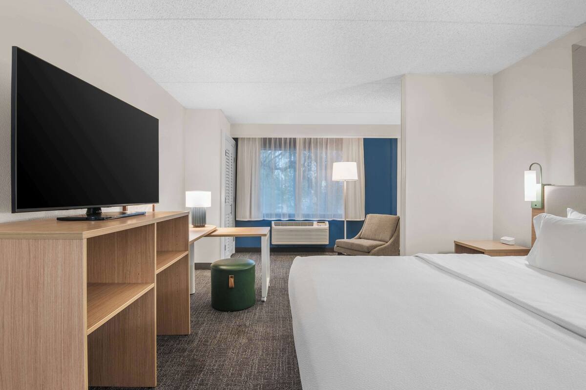 A hotel room with a bed, a desk, a television, a chair, and a lamp.