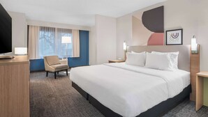 A hotel room with a large bed, a desk, a chair, and a window with curtains. - Spark by Hilton St. Augustine Historic District (St. Augustine)
