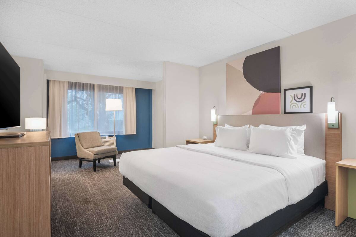 A hotel room with a large bed, a desk, a chair, and a window with curtains.