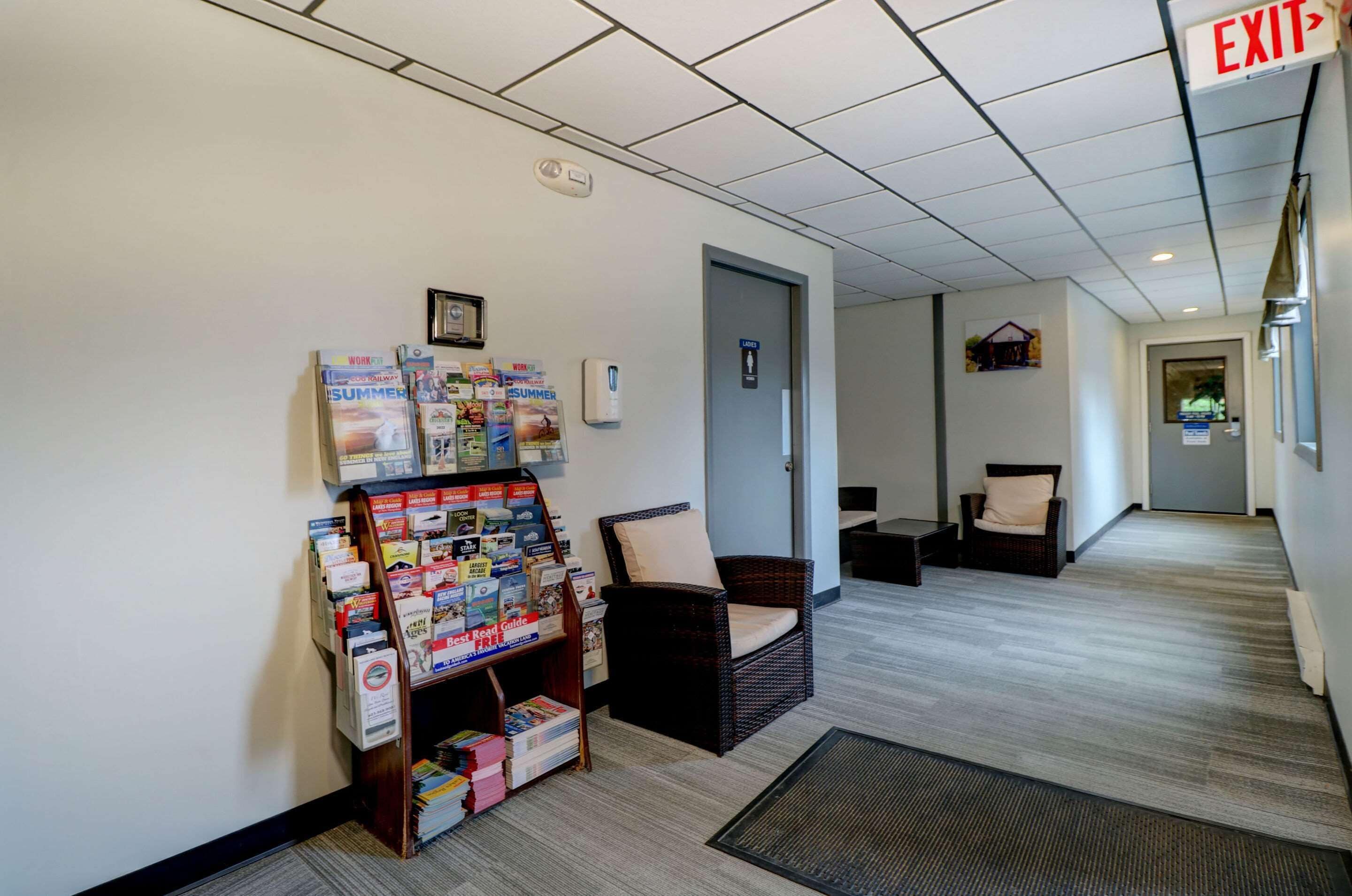 Un área de recepción con un perchero para revistas, una silla de mimbre y una mesa de recepción.