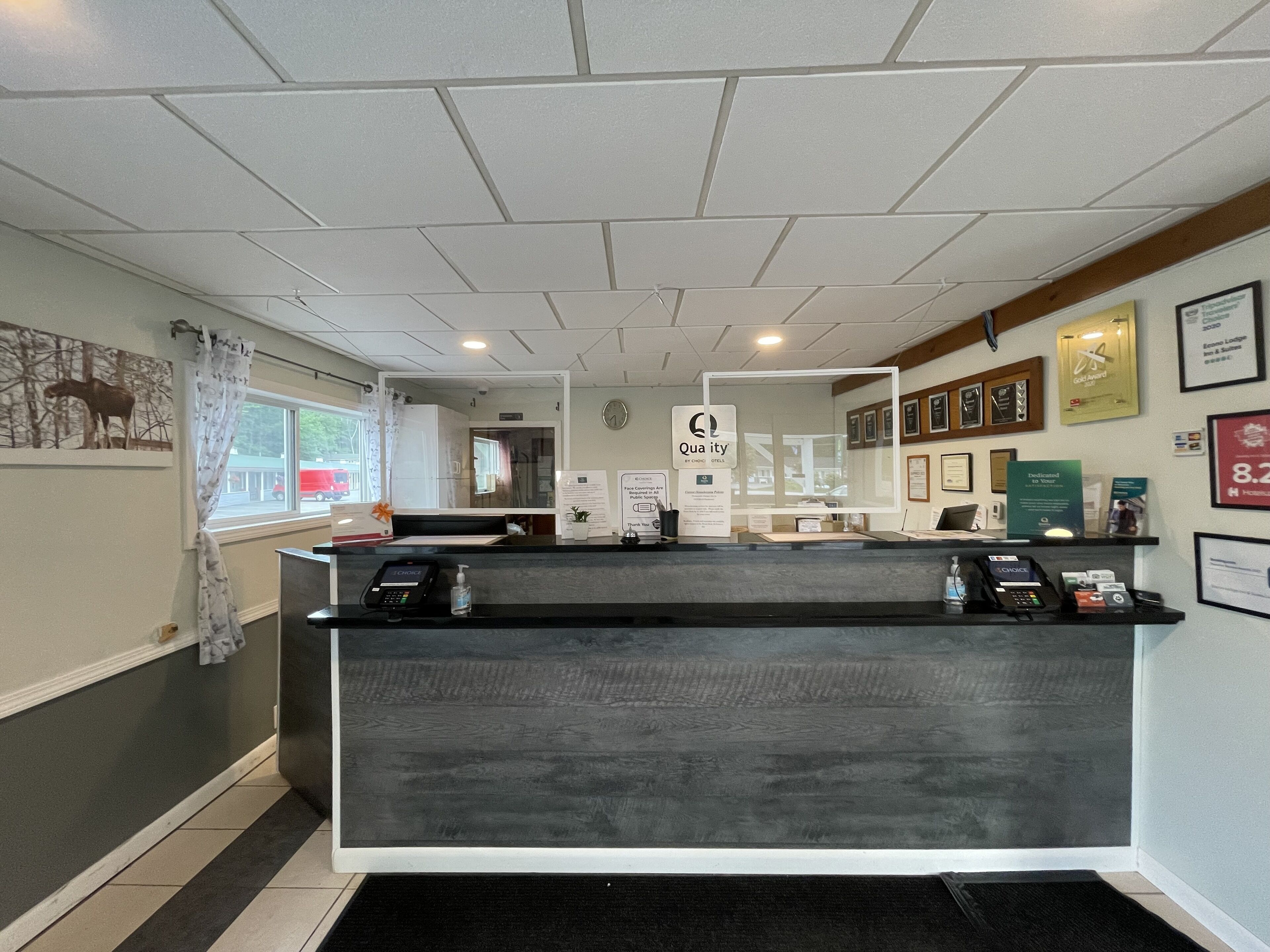 Una reception con una postazione di check-in digitale, premi incorniciati al muro e un orologio.
