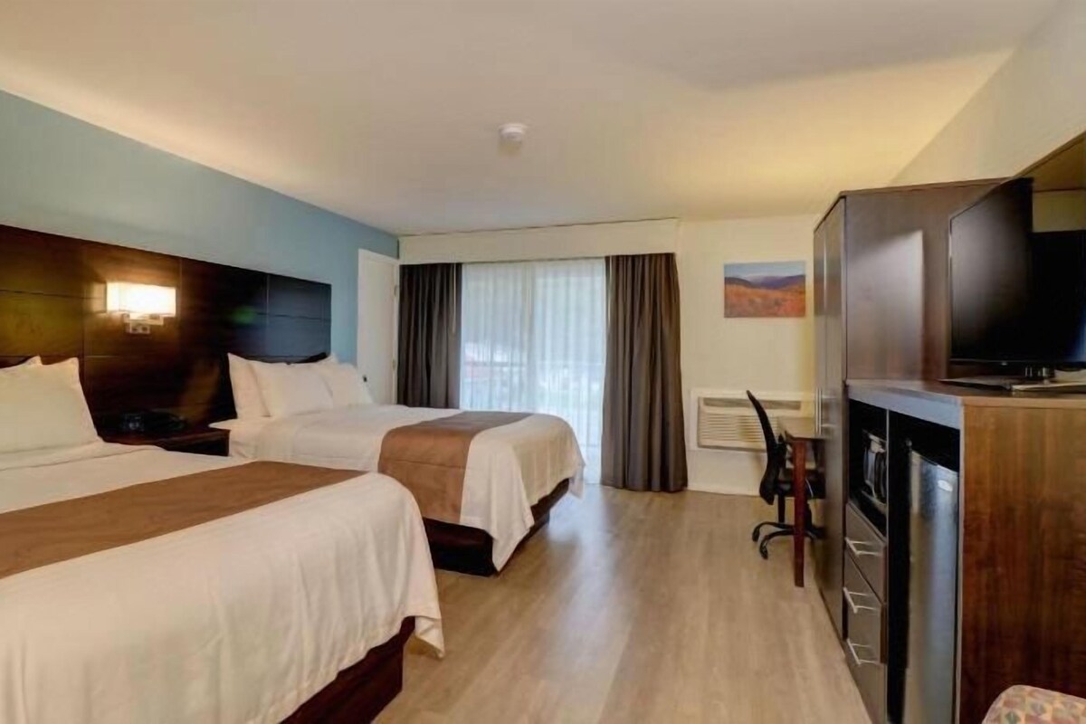 Habitación de hotel con dos camas, un escritorio, un televisor y un ventanal con cortinas.