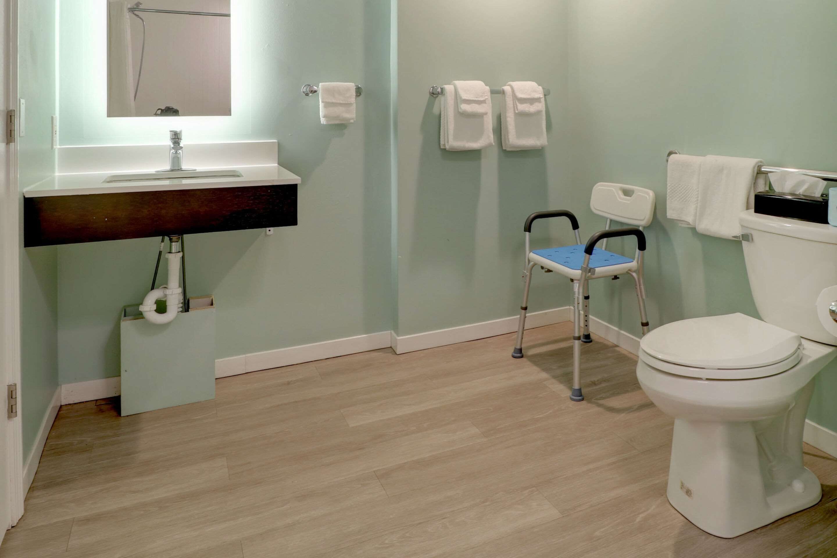 A bathroom with a sink, mirror, toilet, and a wheelchair.