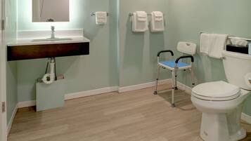 A bathroom with a sink, mirror, toilet, and a wheelchair.