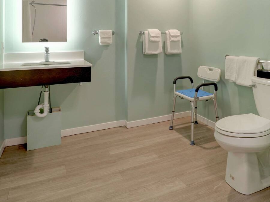 A bathroom with a sink, mirror, toilet, and a wheelchair.