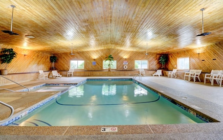 An indoor swimming pool with a wooden ceiling, lounge chairs, and a sign indicating a 3ft depth.