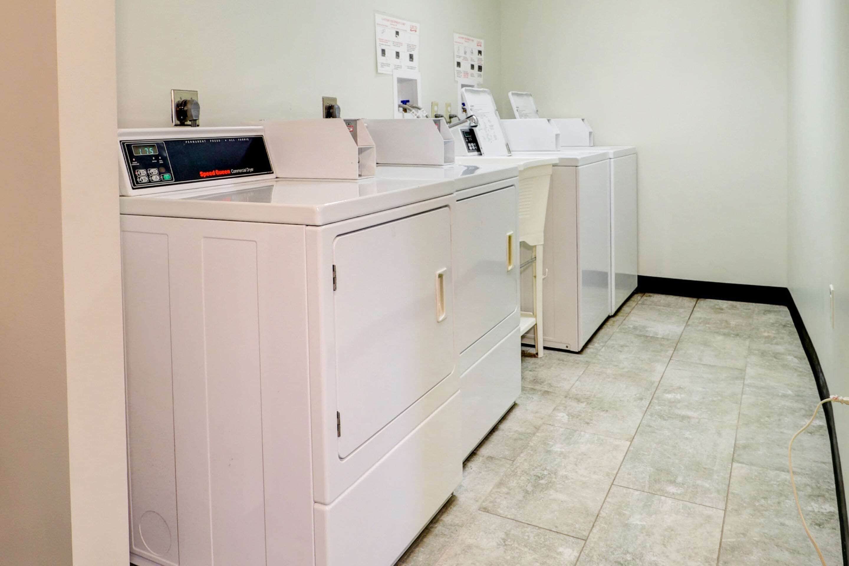 A laundry room with a front-loading washer and dryer, a control panel, and a wall-mounted drying rack.