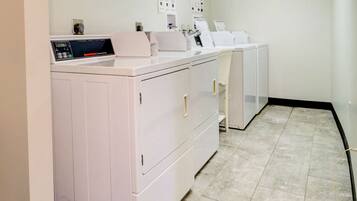 A laundry room with a front-loading washer and dryer, a control panel, and a wall-mounted drying rack.