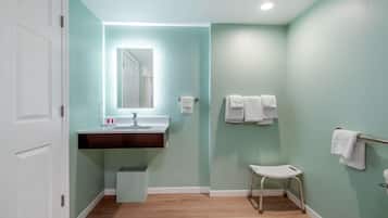 Une salle de bain avec une porte blanche, un lavabo avec un miroir, un petit tabouret et deux porte-serviettes.
