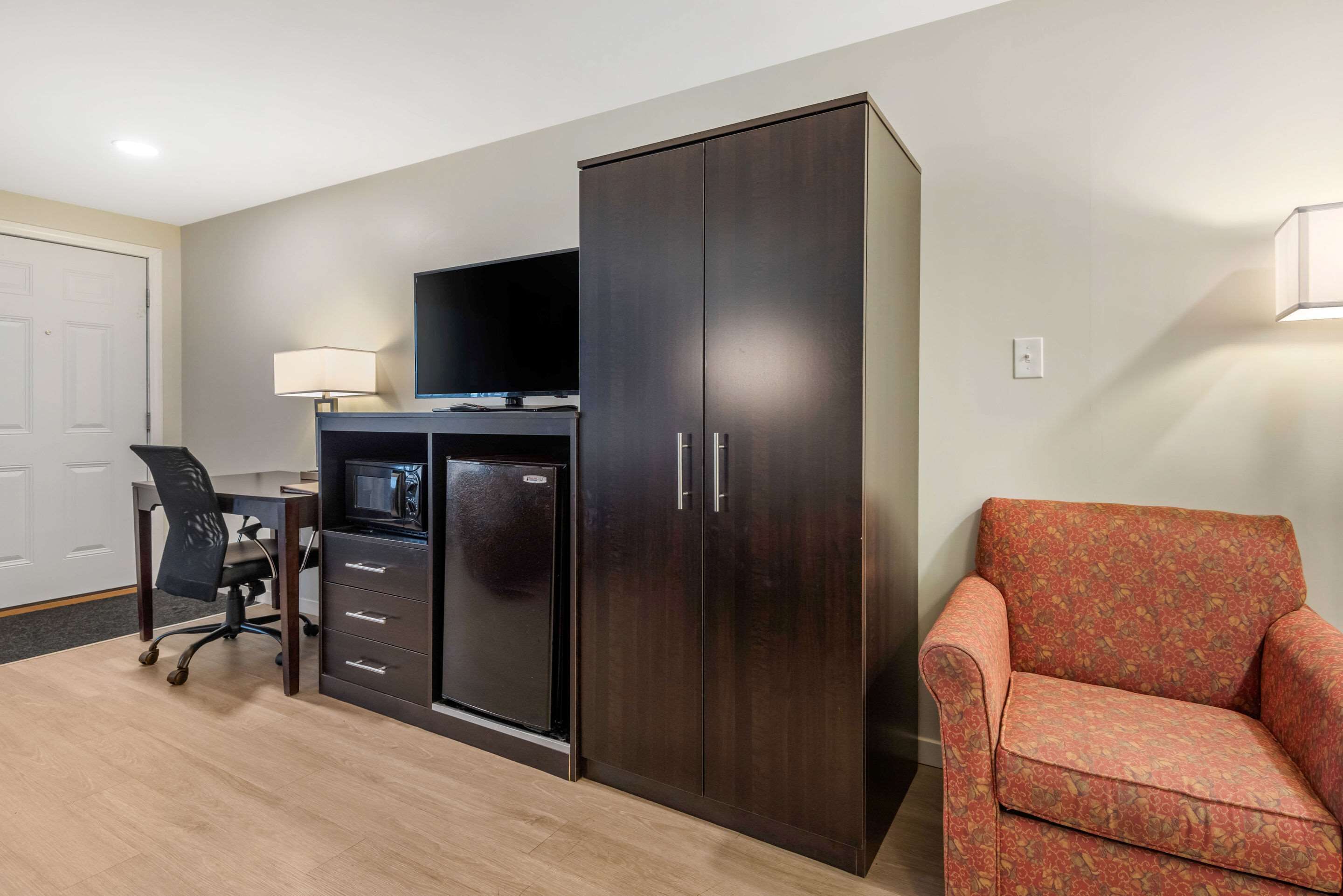 Habitación de hotel con escritorio, un armario amplio, televisor, sillón estampado y lámpara.