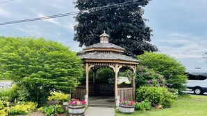 A wooden gazebo with a tiled roof, surrounded by lush greenery and flowering plants. - Quality Inn & Suites Lincoln I-93 (Lincoln)