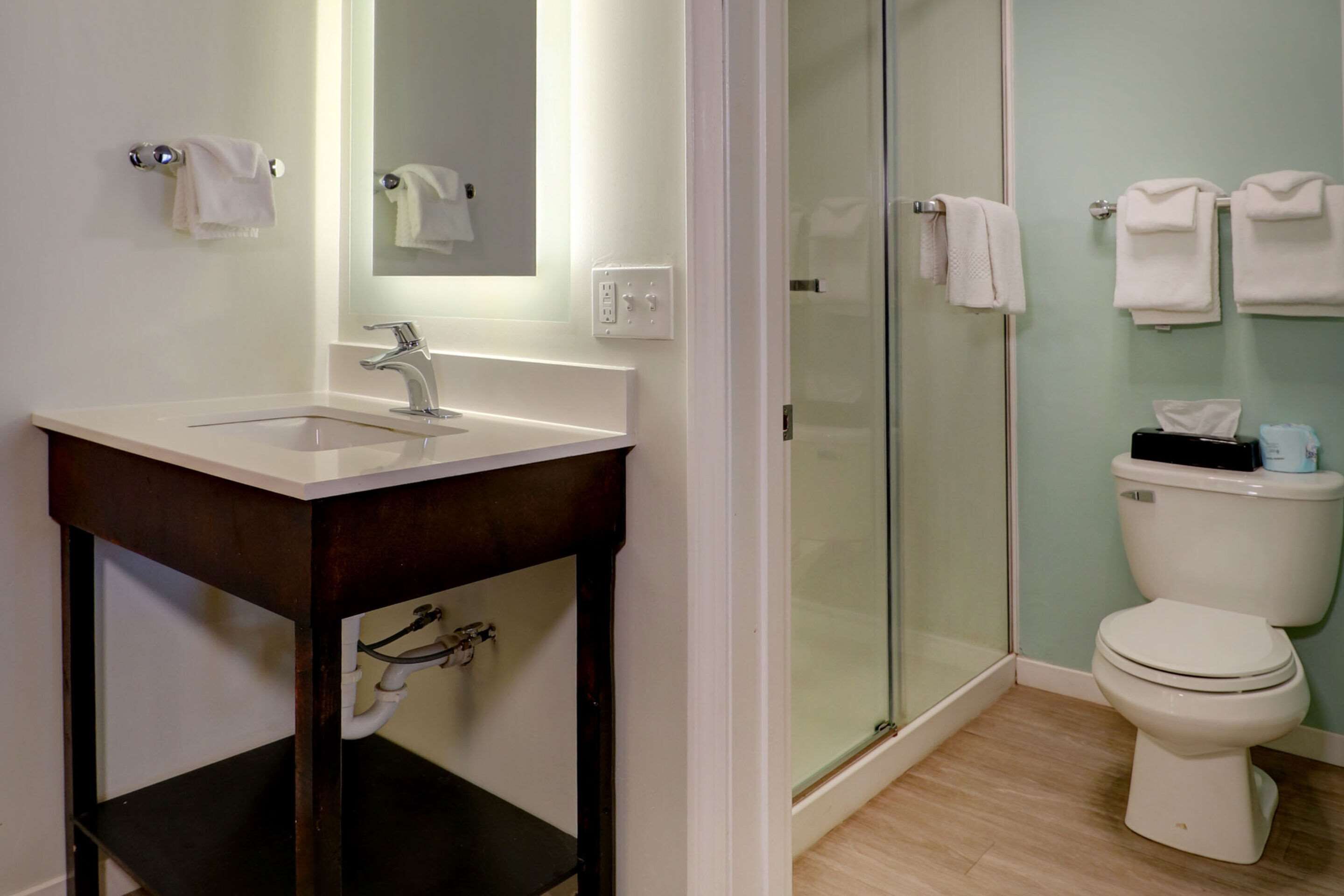 A bathroom with a sink, mirror, glass shower enclosure, toilet, and towels.