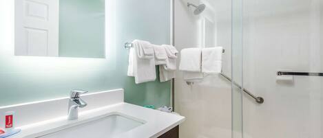 Un baño con lavabo blanco, espejo y ducha con mampara de vidrio.
