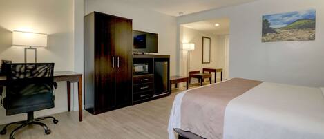 A hotel room with a bed, desk, chair, TV, wardrobe, and a painting on the wall.
