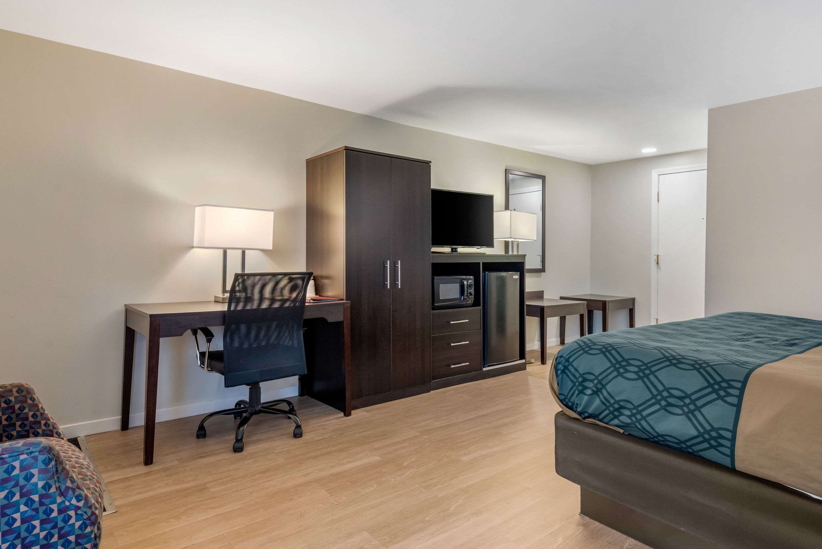 A hotel room with a bed, desk, chair, wardrobe, TV, and a microwave.