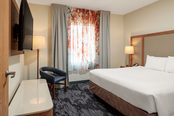 Une chambre d’hôtel avec un lit, un bureau, une chaise, une télévision et une fenêtre avec des rideaux.