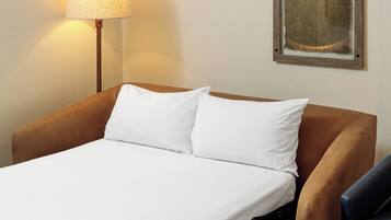 A neatly made bed with white linens, a brown headboard, and a lamp to the left.