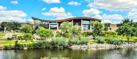 A modern building with a curved roof, surrounded by a well-maintained garden and a pond.