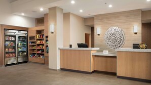 A reception area with a counter, a decorative wall piece, and a refrigerated display with snacks. - Fairfield Inn & Suites by Marriott San Angelo (San Angelo)