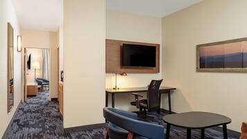 A hotel room with a desk, chair, TV, and a painting on the wall.