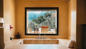 Ένα μπάνιο με ένα μεγάλο παράθυρο, έναν νιπτήρα και θέα σε ένα ορεινό τοπίο.