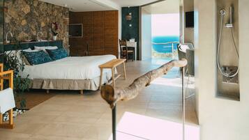 A modern bedroom with a large bed, a desk, and a view of the sea.