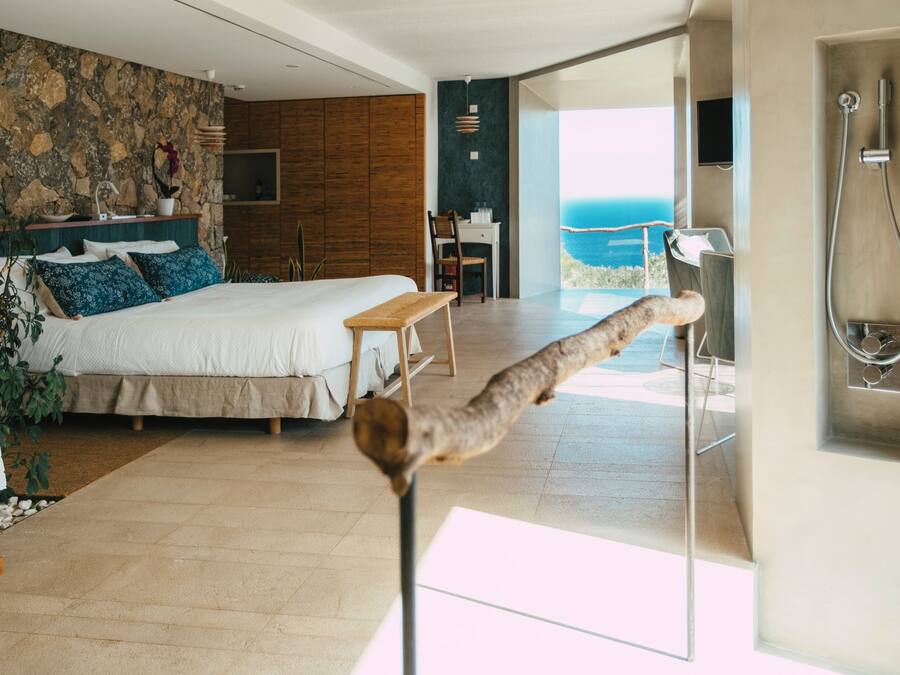 A modern bedroom with a large bed, a desk, and a view of the sea.