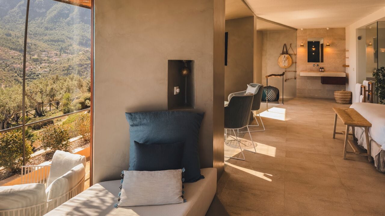 A modern bedroom with a large window overlooking a scenic landscape, a cozy seating area with a sofa and chairs, and a minimalist bathroom with a large mirror and sink.