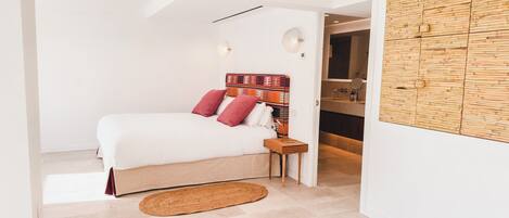 A modern bedroom with a bed, a wooden headboard, a bedside table, and a bathroom visible through an open door.