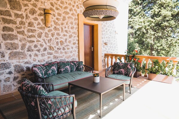 A stone-walled room with a sofa, two chairs, a table, and a hanging light fixture.