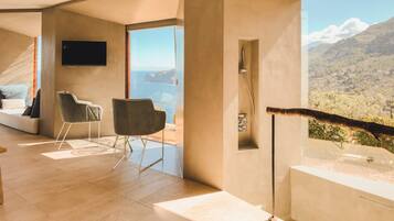 A modern room with a large window, a flat-screen TV, and a seating area with two chairs.