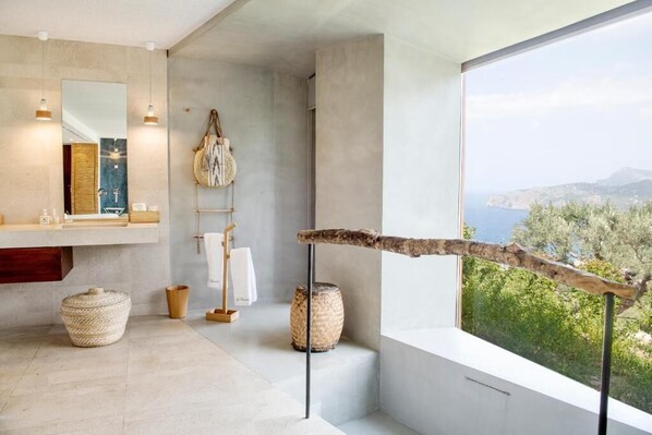 A modern bathroom with a large window, a hanging towel rack, and a rustic branch decoration. - Sa Pedrissa Agroturismo – Adults Only (Deià)