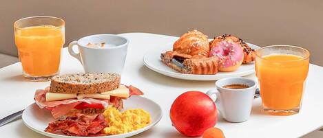 Una mesa de desayuno con tostadas, huevos revueltos, tocino, una manzana roja, albaricoques, pasteles y jugo de naranja.