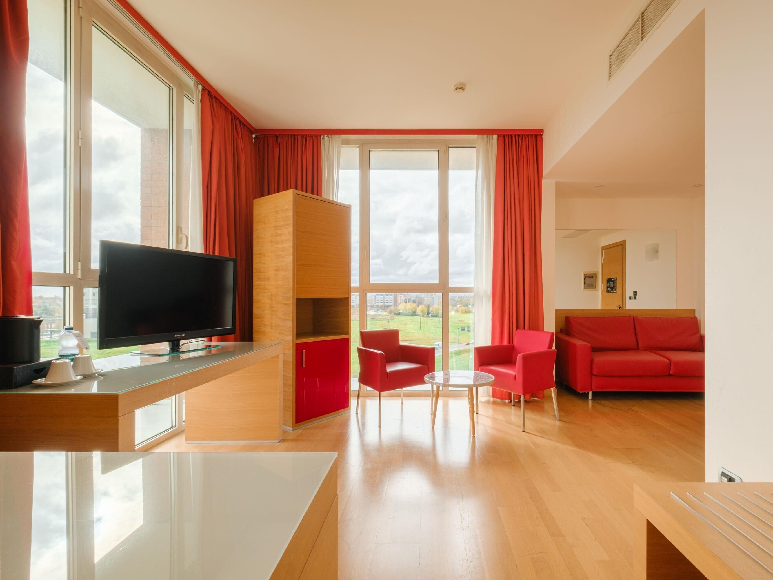 Un soggiorno moderno con televisore a schermo piatto, arredamento rosso e ampie finestre con vista sull'esterno.