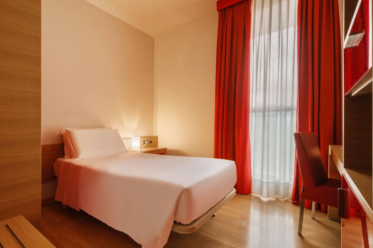Una habitación de hotel moderna con una cama, una mesita de noche, un escritorio y una silla.