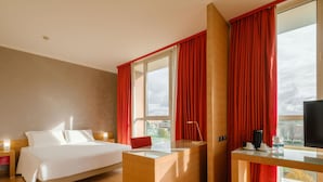 Une chambre d’hôtel avec un lit, un bureau, une télévision et une fenêtre avec des rideaux rouges.