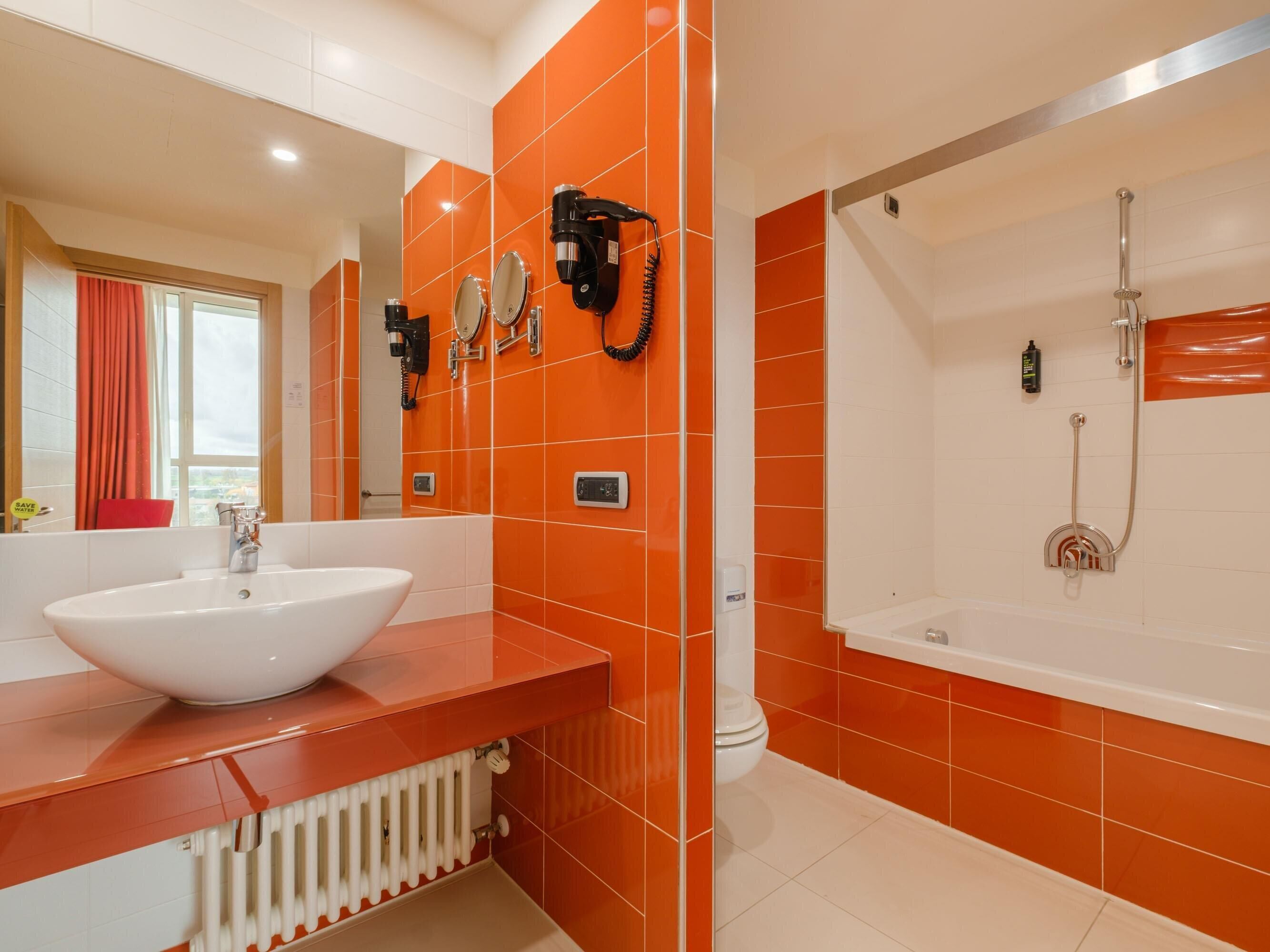 Un bagno moderno con piastrelle arancioni, un lavandino bianco e una vasca da bagno.