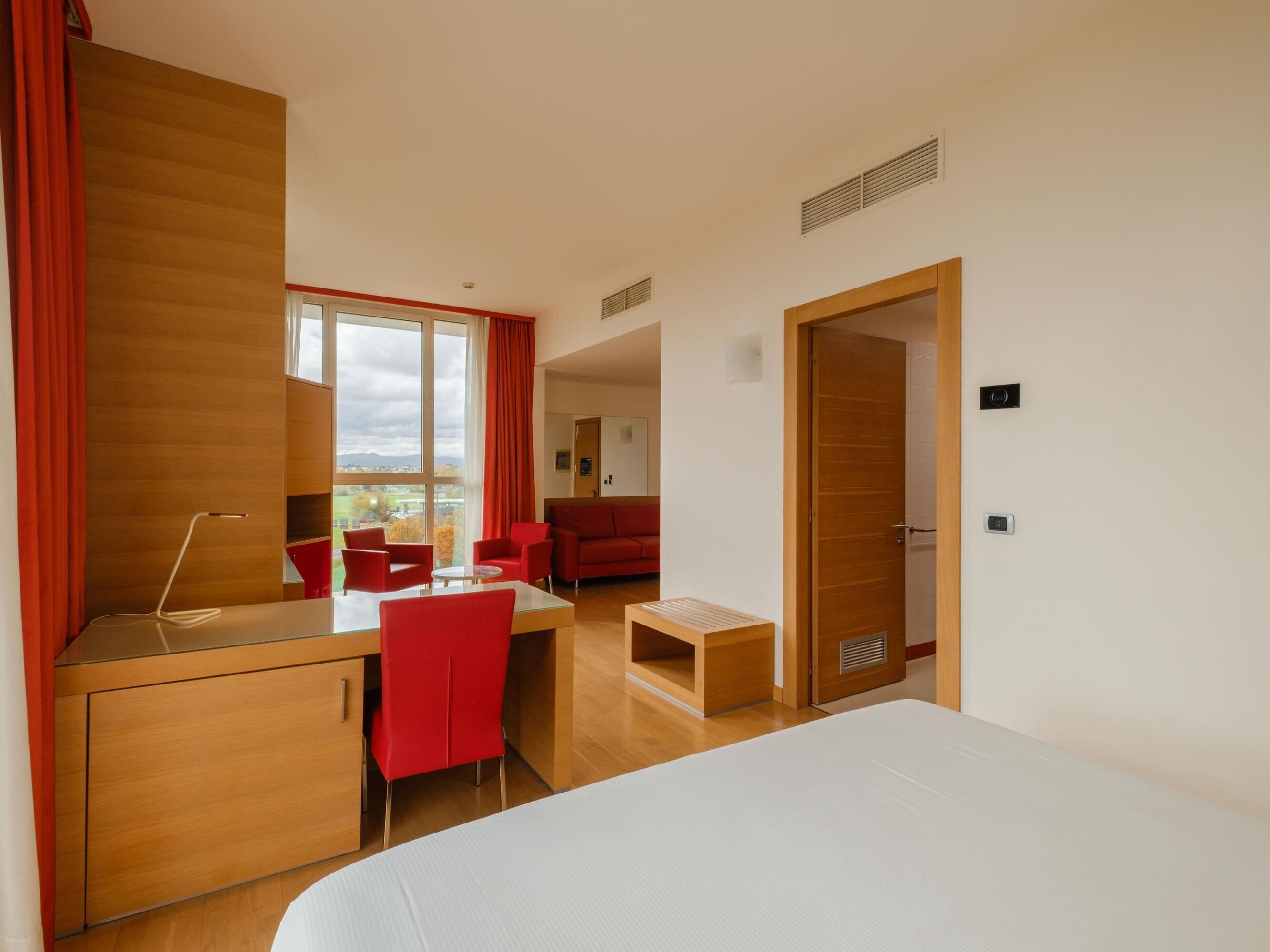 Una habitación de hotel con una cama, un escritorio con una silla, un sofá rojo y una mesita pequeña.