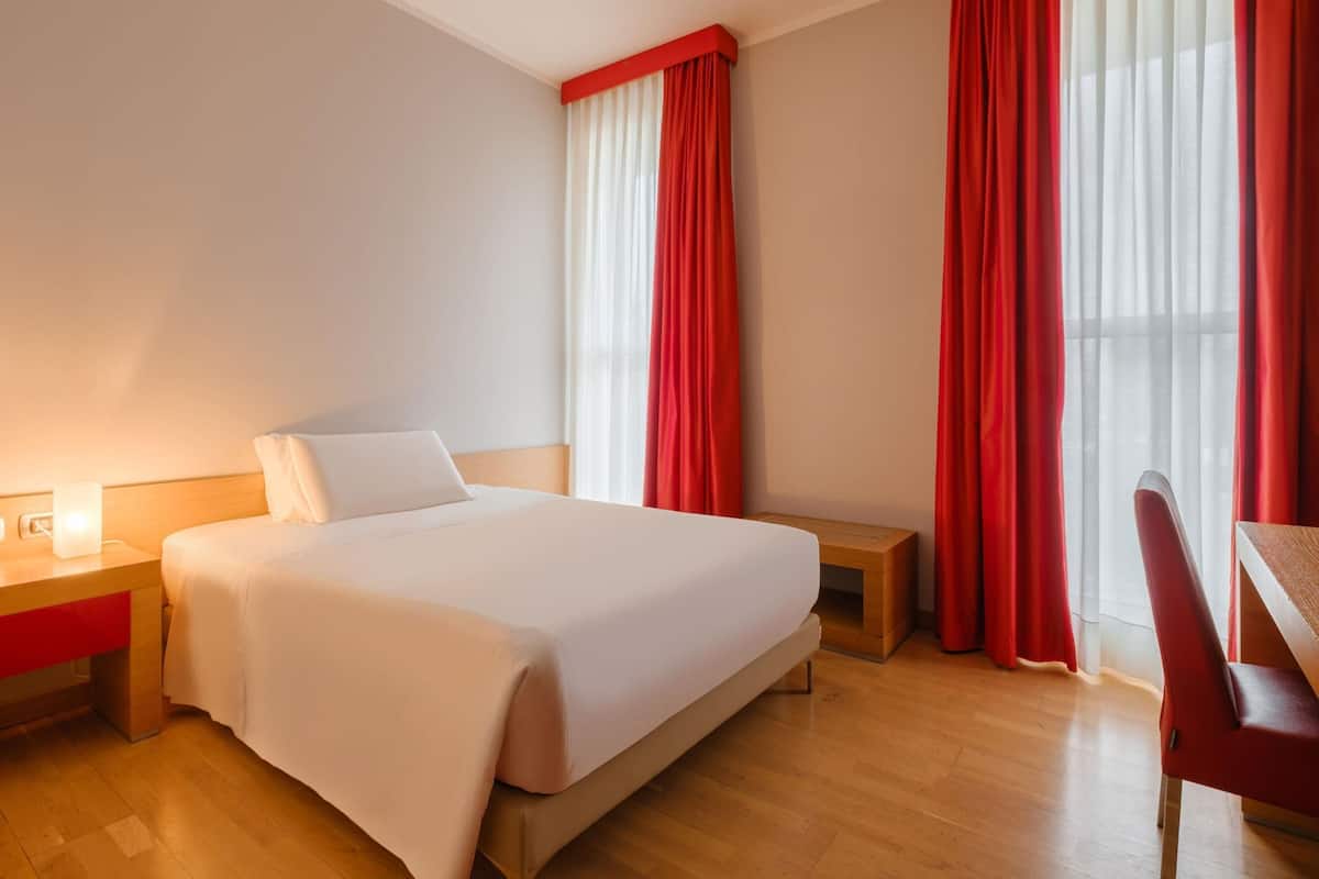 Una habitación de hotel con cama, mesitas de noche, escritorio y una silla.