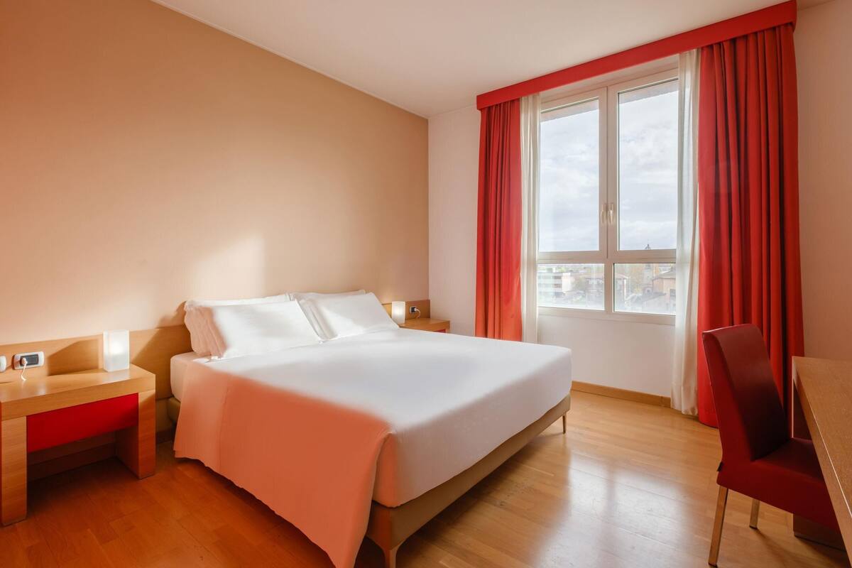 Una habitación de hotel con cama, mesitas de noche, escritorio y silla.