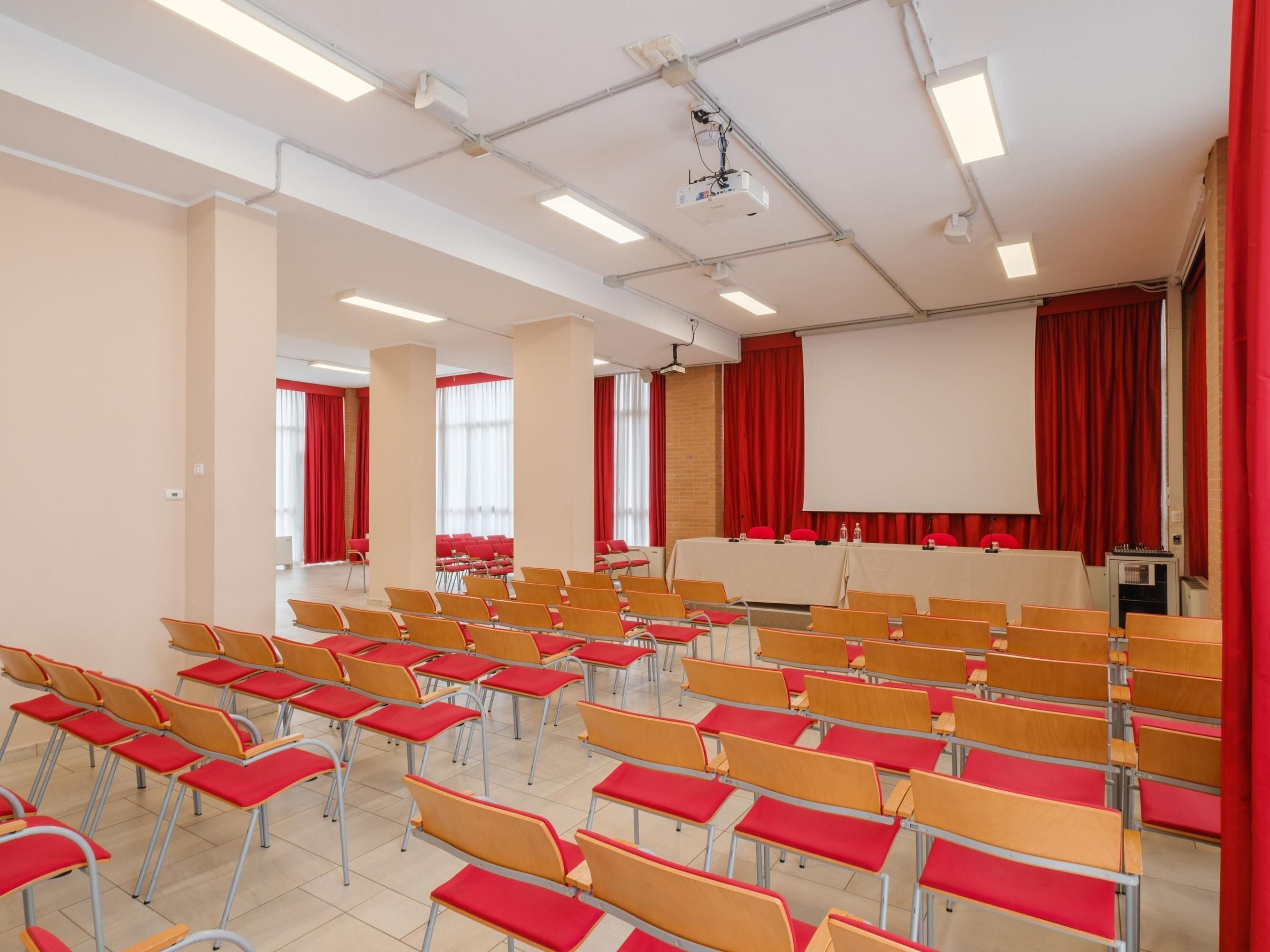 A conference room with rows of chairs, a projector, and a screen.
