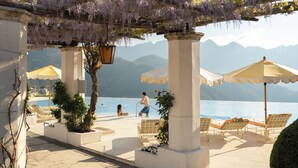 A poolside area with lounge chairs, umbrellas, and a pergola with purple flowers. - Caruso, A Belmond Hotel, Amalfi Coast (Ravello)