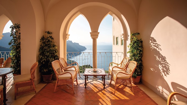 A balcony with wicker furniture, potted plants, and a view of the sea.