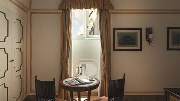 A room with a round table, two chairs, a window with curtains, a wall-mounted lamp, and framed pictures.